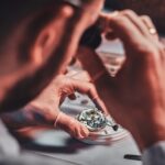 Mature clockmaster is fixing old watch for a customer at his busy repairing workshop